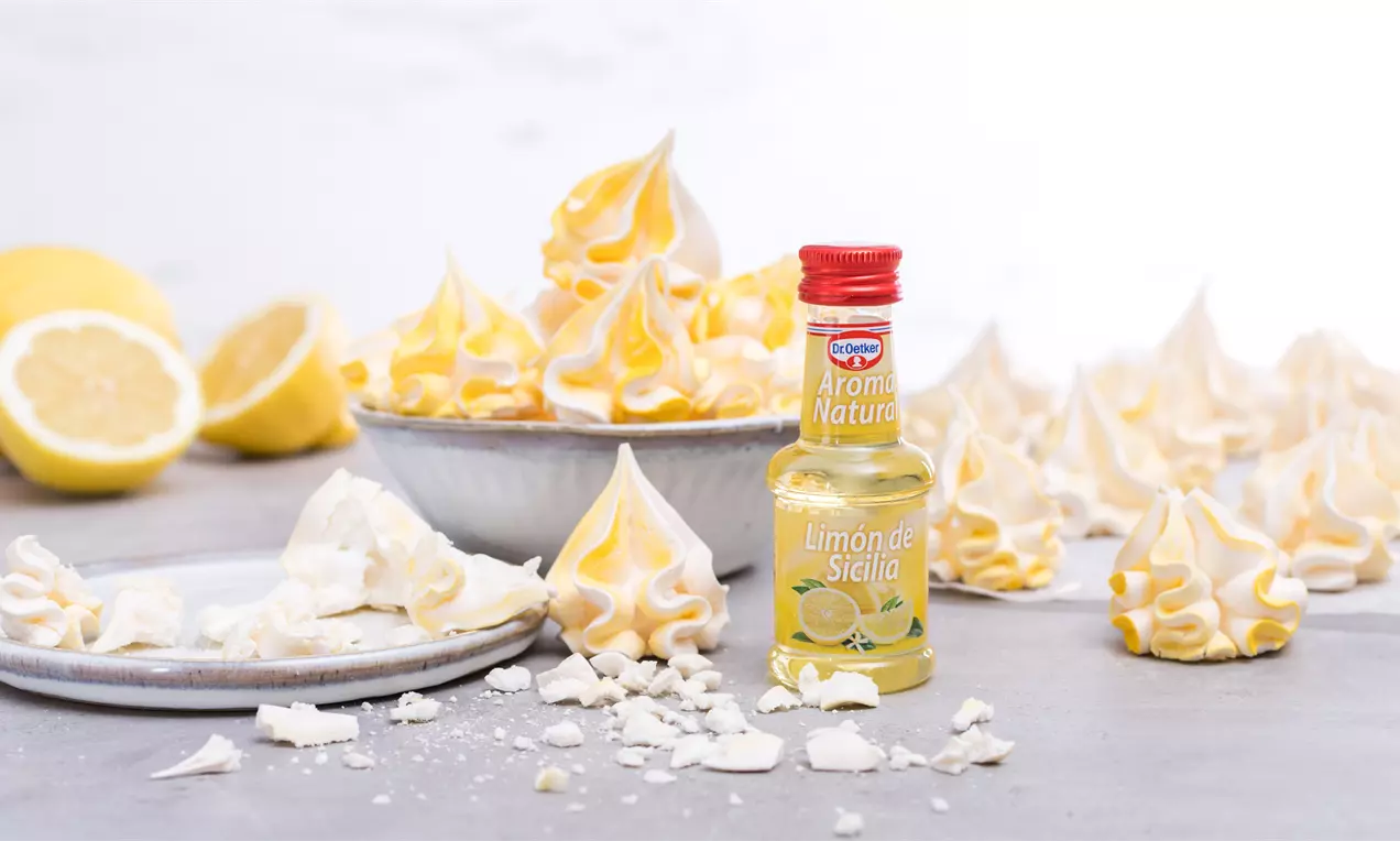 Merenguitos de limón amarillo y blanco con forma espiralada, textura ligera y crujiente, esparcidos junto a rodajas y aroma de limón sobre una mesa