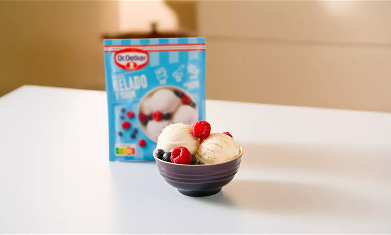 Helado cremoso blanco en un cuenco oscuro acompañado de frutos rojos como cerezas y arándanos en una mesa blanca