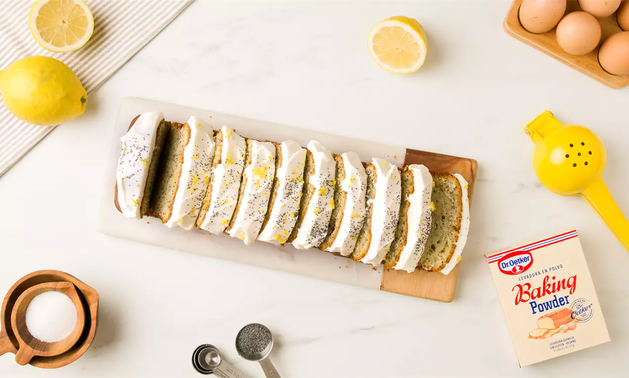 Bizcocho dorado de yogur cortado en rebanadas cubiertas de glaseado blanco, espolvoreadas con semillas de amapola y ralladura de limón amarillo sobre una tabla