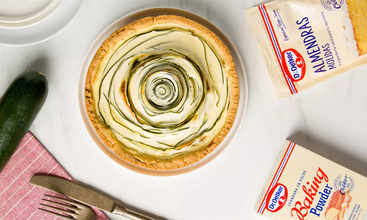 Tarta de masa dorada con finas láminas de calabacín verde dispuestas en espiral sobre un relleno claro en un plato blanco