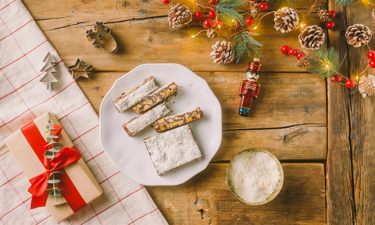 Trozos rectangulares de turrón de chocolate oscuro con frutos secos visibles, espolvoreados con azúcar glas, dispuestos en un plato blanco