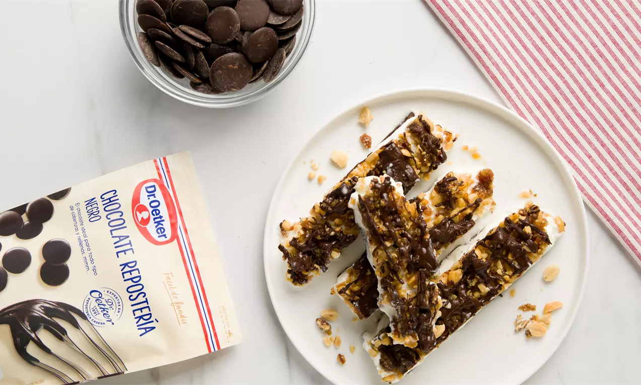 Barritas alargadas con base blanca y superficie irregular de chocolate oscuro y trozos de cacahuetes servidas en un plato blanco
