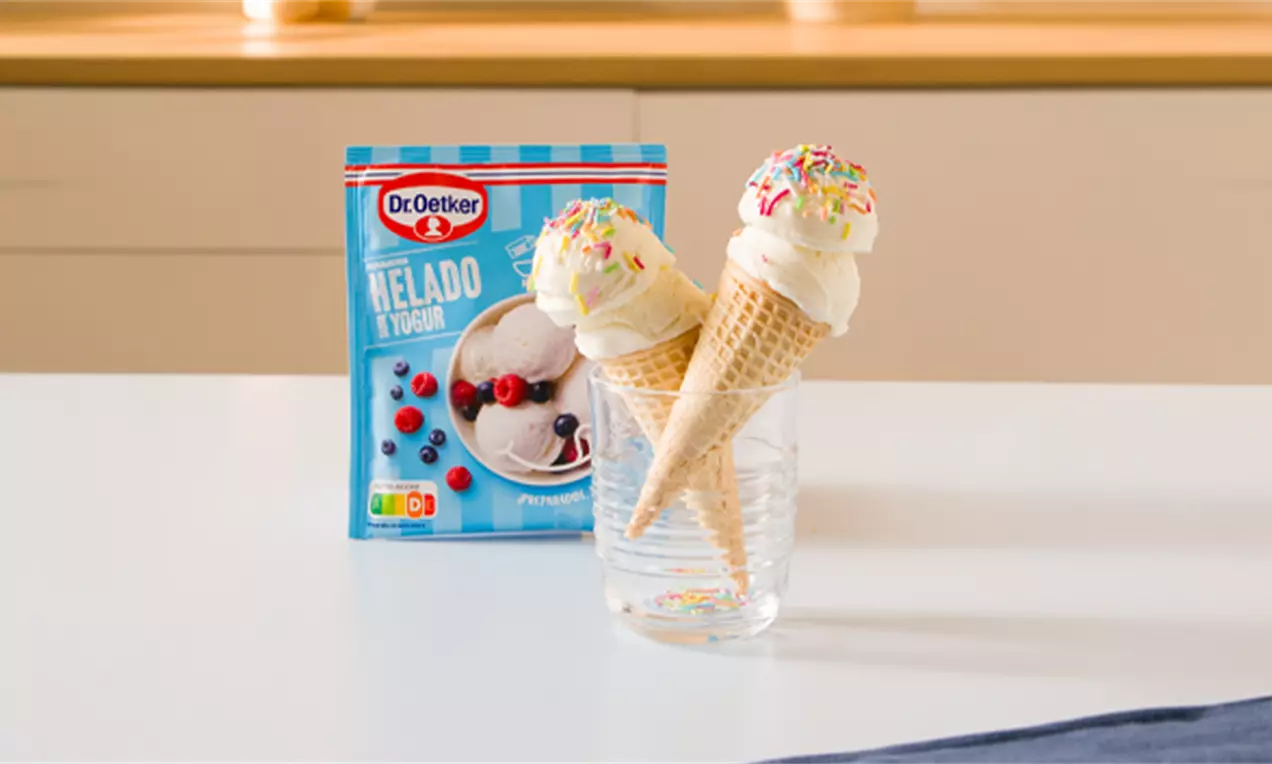 Conos de helado cremoso blanco coronados con chispas de colores, dispuestos en un vaso transparente sobre una mesa blanca